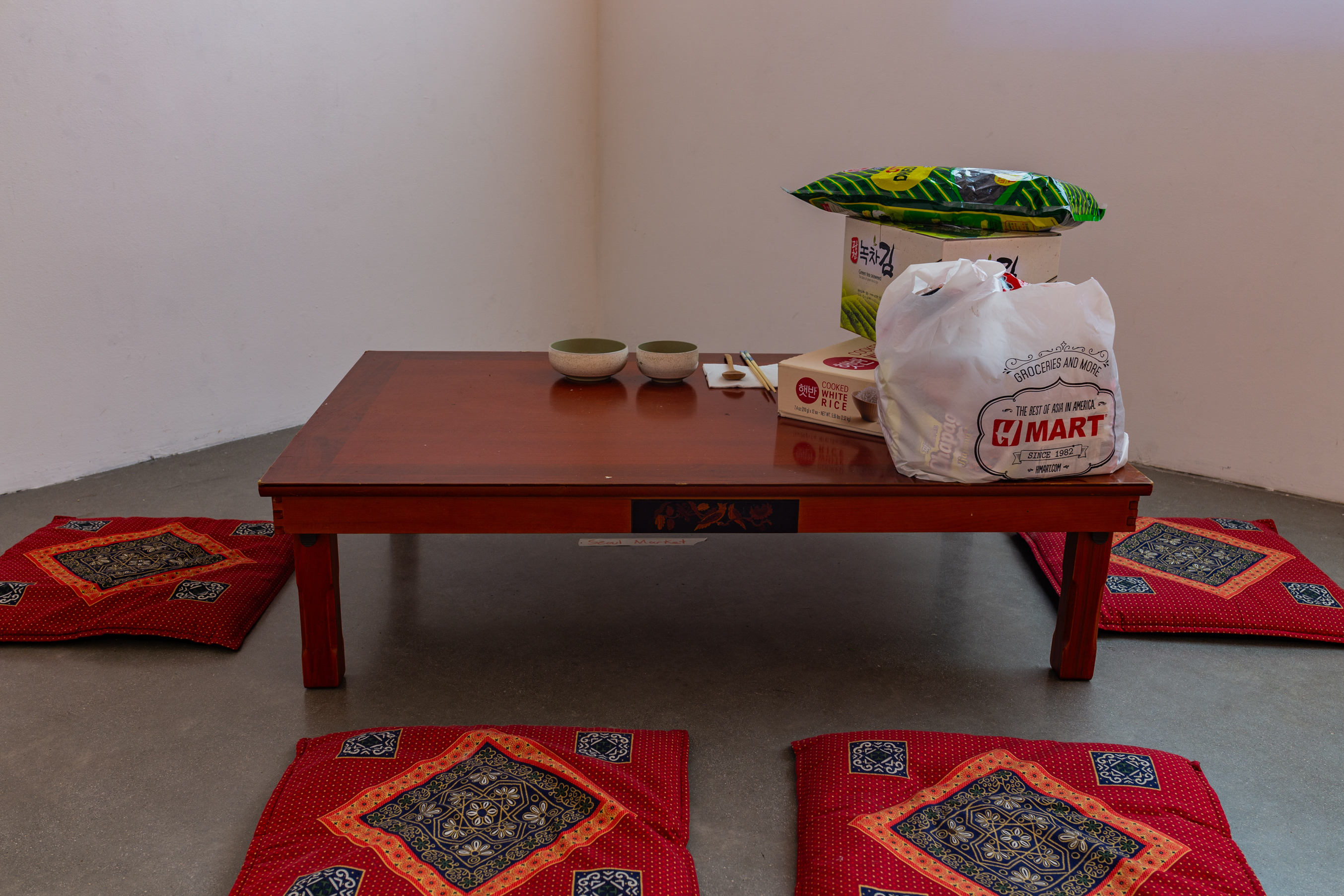 A dark white room with a low table on the left, with 6 seat cushions. On the table are groceries and two bowls.